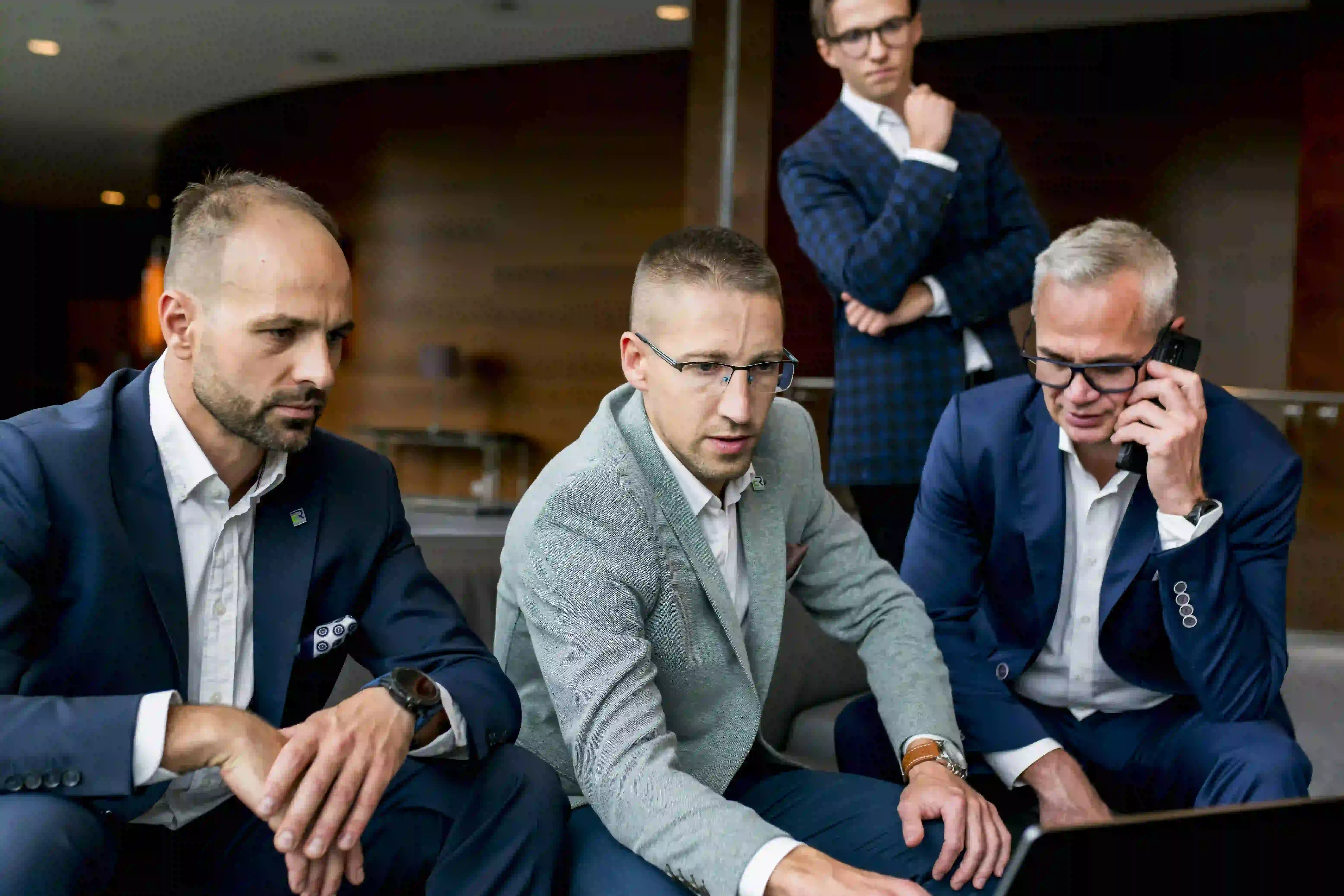 a group of men sitting in a room looking at a laptop